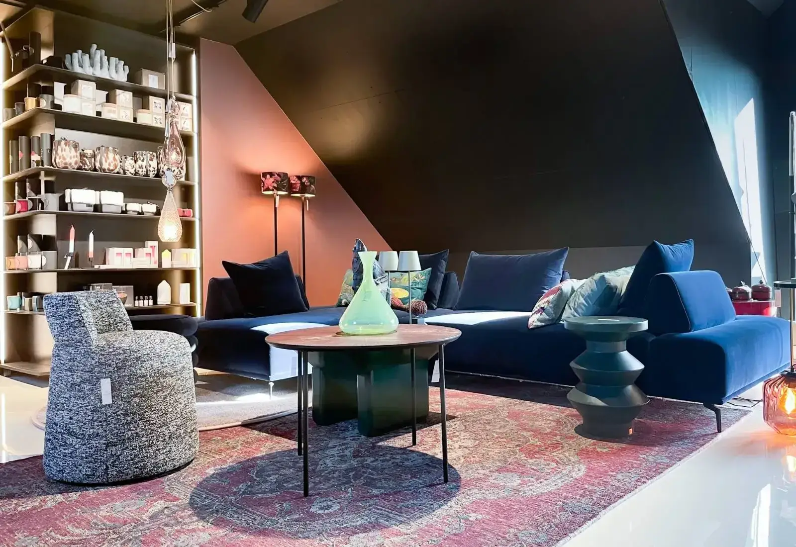 Showroom mit blauem Samtsofa, grüner Glasvase von Nason Moretti auf dem Couchtisch und Regal mit Wohnaccessoires